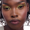 Dragon’s Keep ColourPop Crème Gel Liner creating bold lime‑green and rusty‑red graphic wings with inner‑corner dots on a close‑up model’s eyes, showcasing rich pigment and long‑wear detail against glowy skin in a studio shot.