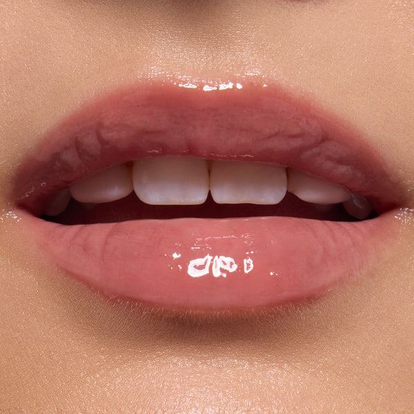 Glossy, close-up lips wearing ColourPop Ultra Glossy Lip in Totally Swamped, a sheer pink-nude shade, catching light with a glassy finish; teeth softly visible in an extreme macro beauty shot against natural skin.