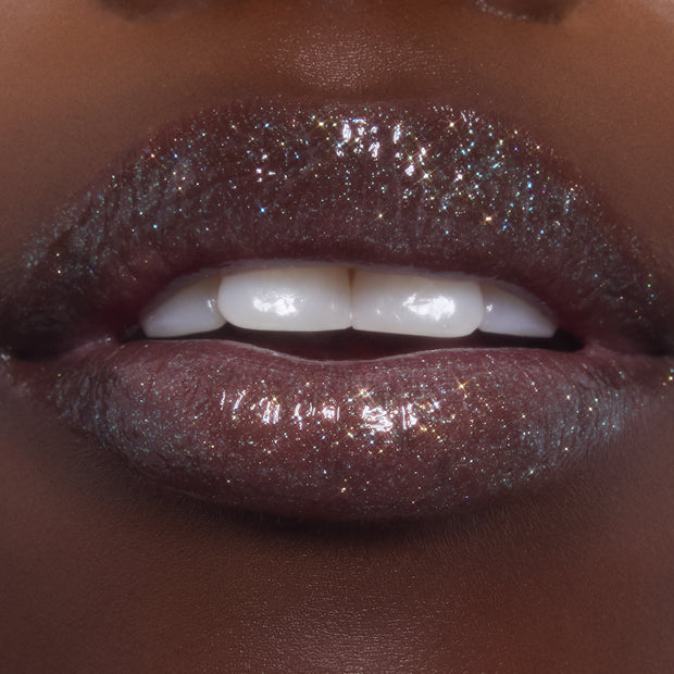 Shimmering lips wearing ColourPop Ultra Glossy Lip in Totally Swamped, a deep cool-toned gloss packed with multicolor sparkle, shown in an extreme close-up as the model parts their lips to reveal a high-shine, wet-look finish.