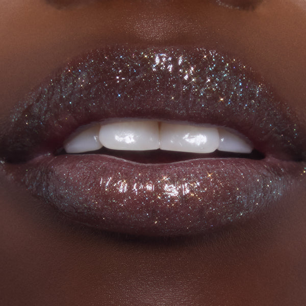 Lips wearing ColourPop Ultra Glossy Lip in Ogre, catching light with multi-dimensional shimmer and glassy shine as teeth gently show; studio macro highlights the deep plum base packed with fine glitter.