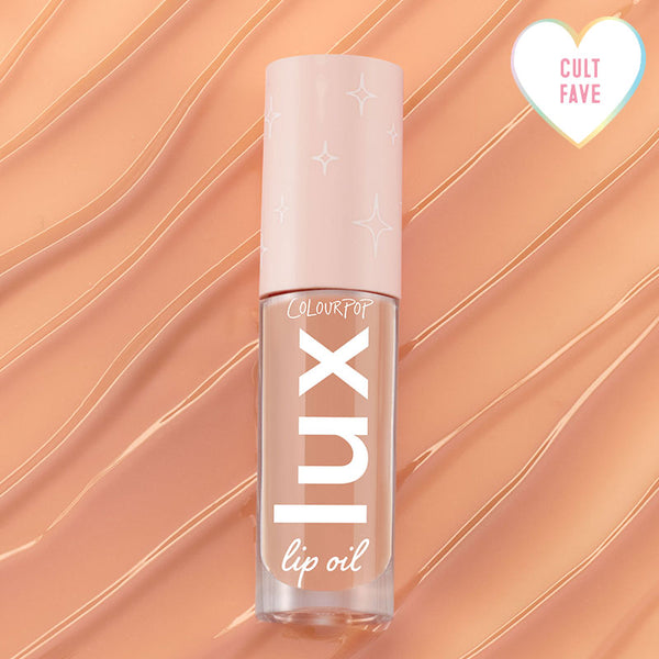 ColourPop Lux Lip Oil Skinny Dip tube resting on glossy peach swirls, showcasing a clear bottle with vertical 'lux' logo and pale pink cap with star motifs, plus a heart 'Cult Fave' badge in the corner.