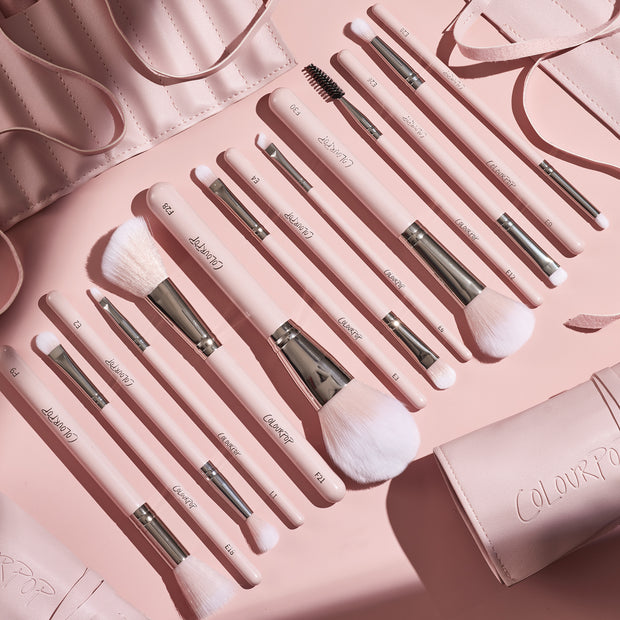 Smoke 'N Roses Brush Roll displaying a full ColourPop Makeup Brush Kit: pink-handled powder, blush, eyeshadow, angled liner, and spoolie brushes with silver ferrules, arranged in a flat lay beside a blush-pink roll-up case embossed ColourPop.