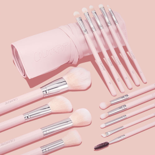 Smoke 'N Roses Brush Roll showcasing a ColourPop Makeup Brush Kit: pink-handled face and eye brushes with soft blush bristles and silver ferrules, plus spoolie and angled liner, fanned from a blush roll embossed ColourPop on a pastel pink background.