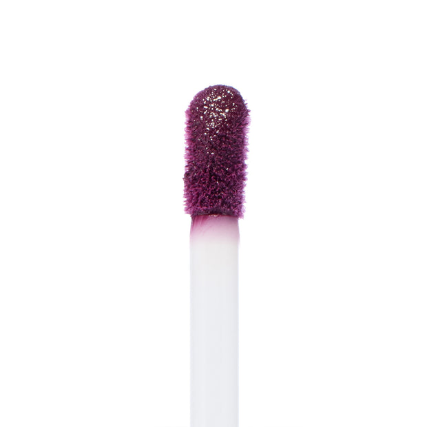 Doe-foot applicator coated in So Vintage, a deep berry-plum ColourPop Ultra Blotted Lip, lifting pigment with a soft, fuzzy tip against a white background, highlighting the saturated color for precise application.