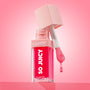 ColourPop So Juicy Plumping Glossy Lip Oil in Flirty Text opens with the doe-foot applicator dripping rosy pink gloss, highlighting the clear square bottle, blush cap, and bold So Juicy logo against a pink gradient studio backdrop.