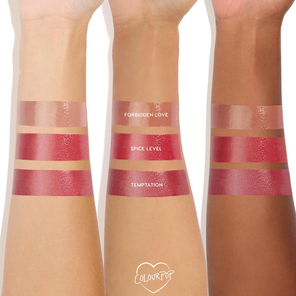 ColourPop So Juicy Plumping Gloss in Spice Level swatched in a bold, glossy stripe on three arms (light, medium, deep), shown between Forbidden Love and Temptation; rich cherry-red tint with a high-shine, plumping finish.