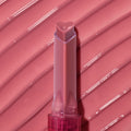 Heart-shaped tip of the Forbidden Love shade glides across a ribbed, glossy rose‑pink swatch, highlighting the shine and creamy payoff of the ColourPop So Juicy Plumping Gloss stick in a clear pink tube.