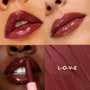 ColourPop So Juicy Plumping Gloss Balm with Peptides in L-O-V-E coats lips in a glossy berry‑plum finish, shown in a four‑panel grid with three model swatches - one applying the stick - and a matching textured smear spelling L‑O‑V‑E.