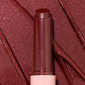 Gloss balm stick twisted up from a pink tube, L-O-V-E shade of the ColourPop So Juicy Plumping Gloss Balm with Peptides, shown close-up against glossy rose-plum shimmer swatches to highlight its dewy, plumping shine and sparkly finish.