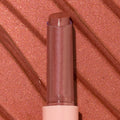 ColourPop So Juicy Plumping Gloss Balm with Peptides in shade Perfection standing upright with bullet extended, a rosy nude shimmer, in a clear cap and blush pink base, shown in macro against a matching metallic swatched background.