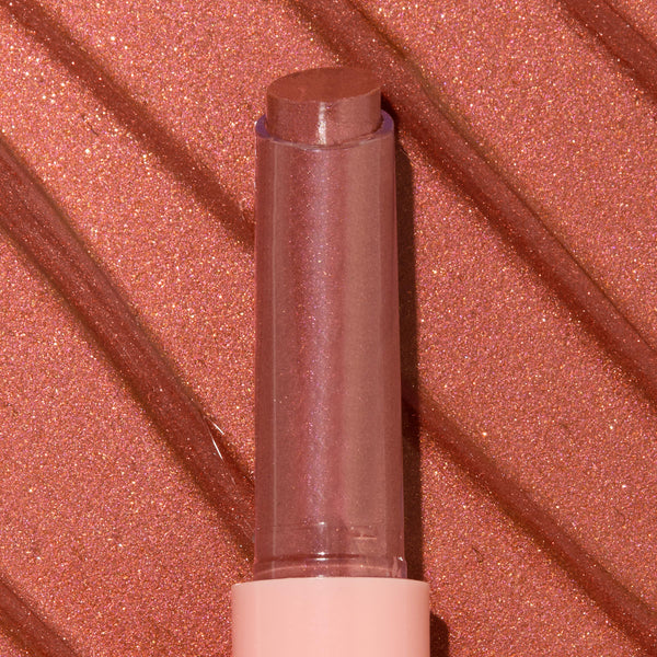ColourPop So Juicy Plumping Gloss Balm with Peptides in shade Perfection standing upright with bullet extended, a rosy nude shimmer, in a clear cap and blush pink base, shown in macro against a matching metallic swatched background.