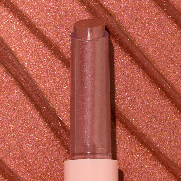 ColourPop So Juicy Plumping Gloss Balm with Peptides in shade Perfection standing upright with bullet extended, a rosy nude shimmer, in a clear cap and blush pink base, shown in macro against a matching metallic swatched background.