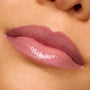 Glossy lips wearing Forbidden Love, a sheer rosy-mauve shade of ColourPop So Juicy Plumping Gloss, reflecting high shine in an extreme close-up swatch that highlights a smooth, hydrated, subtly plumped finish.