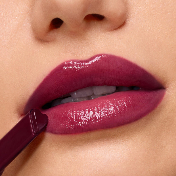 Berry-toned lips wear ColourPop So Juicy Plumping Gloss in Temptation, the heart-tipped applicator gliding on a high-shine, cushy finish; tight macro studio shot highlighting the smooth, plumped look and rich pigment.