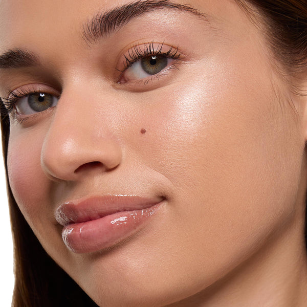 Highlighter glow catching light on cheekbone and brow bone, showcasing Ohana ColourPop Super Shock Highlighter's smooth, dewy finish on a model's skin, with natural makeup and glossy lips in a tight face close-up.