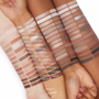 Stone Cold Fox ColourPop Shadow Palette swatches in cool neutrals - ivory, taupe, greige, mauve, silver, charcoal - displayed in neat rows across three arms of light, medium, and deep skin, with labeled shades highlighting matte and shimmer payoff.