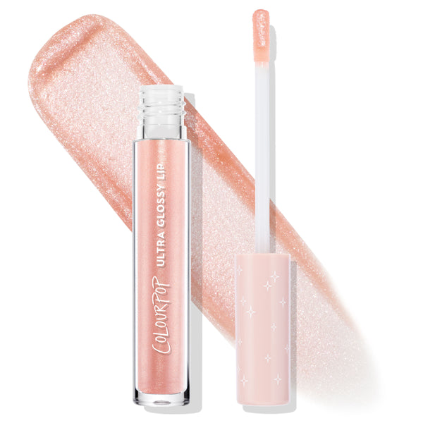 ColourPop Ultra Glossy Lip in Sugar Cookie stands with its wand uncapped, doe-foot applicator coated in peachy nude shimmer, set over a wide swatch of sparkling gloss; clear tube and blush star-print cap highlight the high-shine finish.