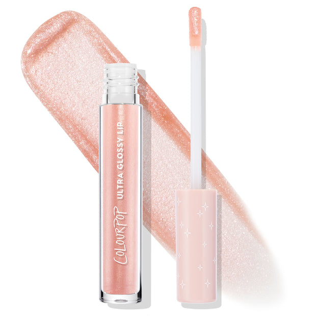 ColourPop Ultra Glossy Lip in Sugar Cookie stands with its wand uncapped, doe-foot applicator coated in peachy nude shimmer, set over a wide swatch of sparkling gloss; clear tube and blush star-print cap highlight the high-shine finish.