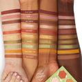 Sweet As Can Bee ColourPop Shadow Palette swatched in clean stripes on three arms from light to deep skin tones, showing matte and metallic hues from honey gold and rust to olive green and pink; shade names labeled on a white studio backdrop with palette corner visible.
