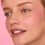 Rosy cheek and soft pink lips glow, showcasing the That’s So Rosy ColourPop Cheek & Lip Set on a close-up model; creamy blush and matching lip tint blend seamlessly with a dewy finish against a pastel pink background.