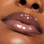 Plum-tinted lips glossed with ColourPop Lux Lip Oil, shade Vampy Lips, gleam with a glassy shine, reflecting light in an extreme close-up on warm brown skin.