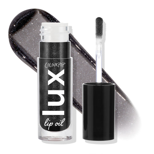 Team Jacob ColourPop Lux Lip Oil displayed open, doe-foot applicator beside the tube and a glossy charcoal-black swatch with silver shimmer behind, highlighting the sheer, high-shine finish; cap off on a white studio backdrop.