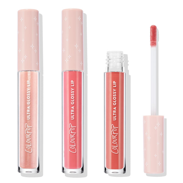 Tickled Pink ColourPop Ultra Glossy Lip trio standing upright, one tube opened with doe‑foot applicator showing rosy pink gloss; shades range from pearly champagne to bright pink to warm rose with blush star‑print caps on a white background.