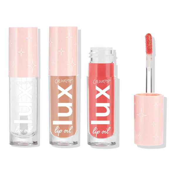 ColourPop Lux Lip Oil Top Hits bundle lined up, three lip oils - clear, warm nude, and coral pink - with pastel pink star-print caps, one tube opened to show the doe-foot applicator, set against a clean white studio background.