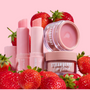 Strawberry ColourPop Lip Balm twisted up in a blush-pink tube, displayed with matching strawberry lip scrub and lip mask jars nestled among ripe strawberries on a pale pink backdrop, highlighting a hydrating, glossy finish and fruity scent.