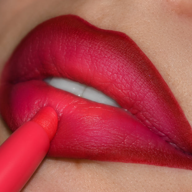Bichette Lippie Pencil lines and fills lips in vivid cherry‑red with pink undertones; close‑up shows the creamy ColourPop Lippie Pencil tip tracing the lower lip for sharp edges and a smooth, matte, smudge‑resistant finish.