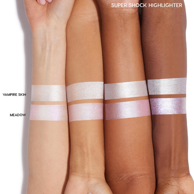 Meadow ColourPop Super Shock Highlighter swatched as iridescent pink‑lavender bands on four arms of varying skin tones, shown under the Super Shock Highlighter header beside the brighter silver‑white Vampire Skin shade for comparison.