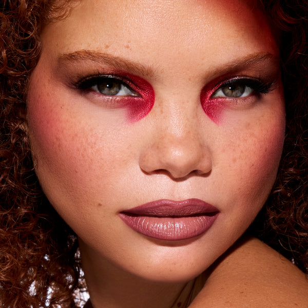 Model wears dramatic red and black smokey eye and mauve lipstick created with The Twilight Saga Eclipse X ColourPop full collection set, showcasing bold Twilight inspired makeup on glowing freckled skin in close-up beauty shot.
