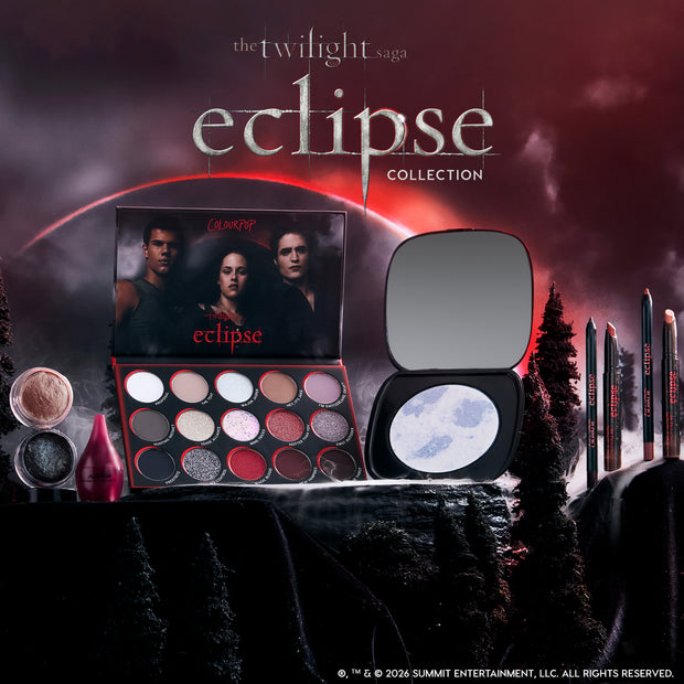 The Twilight Saga Eclipse X ColourPop full collection set displayed against a moody red Twilight sky, featuring an open multi-pan eyeshadow palette, moon-printed highlighter compact, liners, and shimmer pigments styled among dark forest scenery.