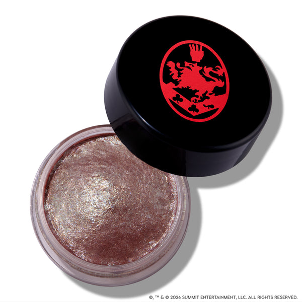 Open ColourPop Cullen Coven Jelly Much Shadow, a shimmery metallic taupe cream eyeshadow inspired by Twilight, sits in a clear round jar with a tilted black lid featuring a bold red crest logo on a white background.