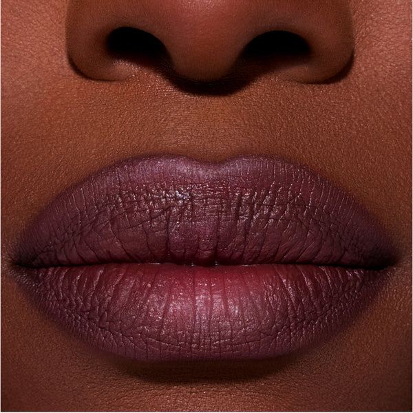 Close-up of full lips wearing ColourPop New Love Lippie Stix in a deep plum Twilight-inspired shade, showing smooth, satin finish color payoff on rich skin tone for a bold, evening makeup look.