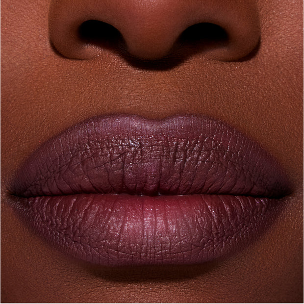 Close-up of full lips wearing ColourPop New Love Lippie Stix in a deep plum Twilight-inspired shade, showing smooth, satin finish color payoff on rich skin tone for a bold, evening makeup look.