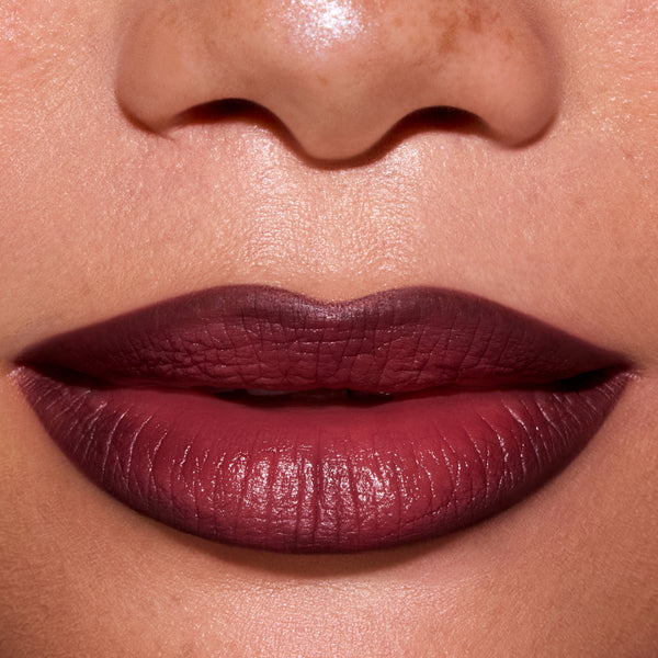 Close-up of a model’s lips wearing ColourPop New Love Lippie Stix, showing a smooth, deep berry-mauve Twilight inspired lip color with a soft satin finish against natural, freckled skin.