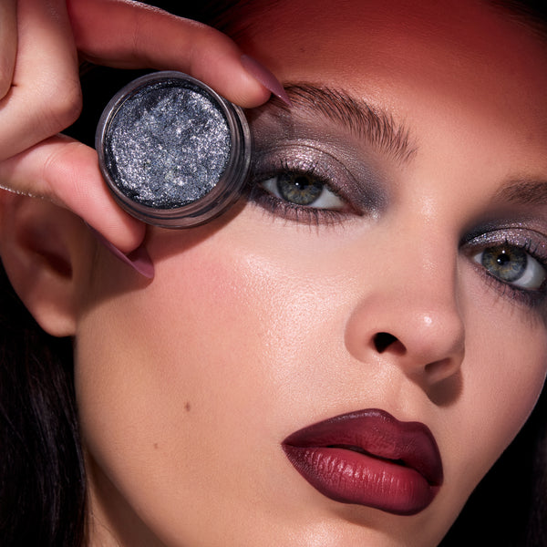 Model holds ColourPop Newborn Army Jelly Much Shadow, a metallic gunmetal shade, beside her twilight-inspired smoky eye makeup, showcasing the product’s wet-look shimmer and intense payoff against bold berry lips.
