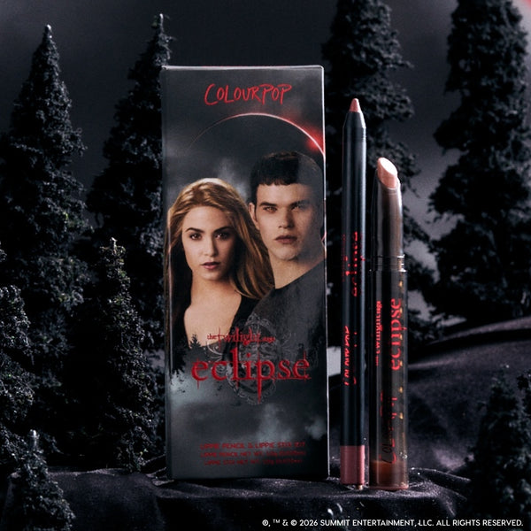 ColourPop Opposites Attract Lippie Stix from the Twilight Eclipse collection standing with matching lip pencil beside character-printed box, styled in a dark, misty forest setting for a dramatic, vampy makeup look.