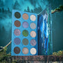 Twilight Forever palette trio display standing open on mossy forest logs, showing 15 cool-toned and shimmery Twilight-inspired eyeshadows in a blue case with character artwork, styled against a misty evergreen Twilight backdrop for dramatic makeup looks.
