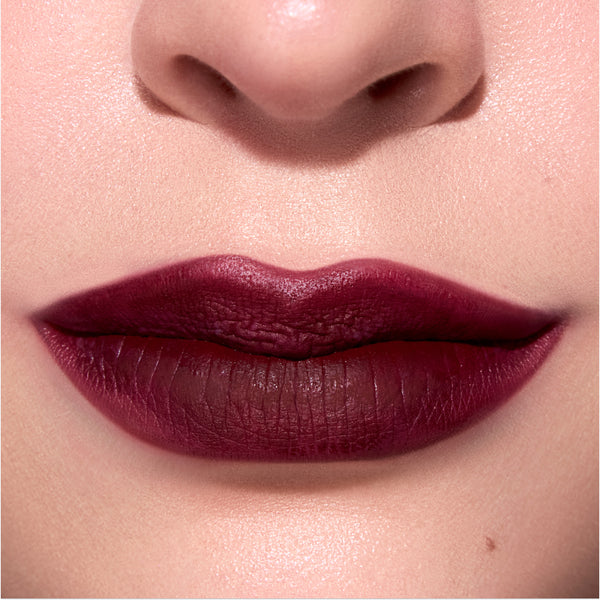 Closeup lips wear Newborn Powder To Creme Lipstick in a deep Twilight-inspired berry shade, showing smooth velvety texture and full coverage color against natural, softly lit skin.