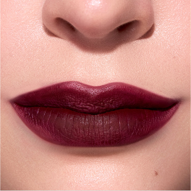 Closeup lips wear Newborn Powder To Creme Lipstick in a deep Twilight-inspired berry shade, showing smooth velvety texture and full coverage color against natural, softly lit skin.