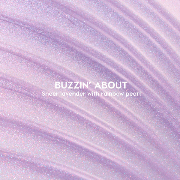 ColourPop Ultra Glossy Lip Buzzin' About swatched - sheer lavender gloss with rainbow pearl shimmer - spread in sweeping ridges across a close-up backdrop to showcase its glossy, sparkly finish.