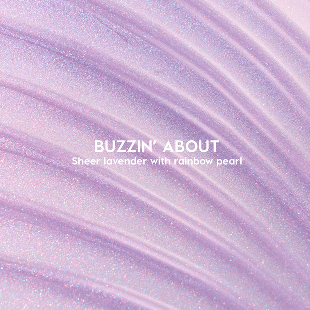 ColourPop Ultra Glossy Lip Buzzin' About swatched - sheer lavender gloss with rainbow pearl shimmer - spread in sweeping ridges across a close-up backdrop to showcase its glossy, sparkly finish.