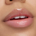 Glossed lips wearing ColourPop Ultra Glossy Lip in Buzzin’ About, a sheer pink gloss with fine iridescent shimmer, reflecting light for a high-shine finish; close-up lip swatch shows smooth, hydrated appearance.