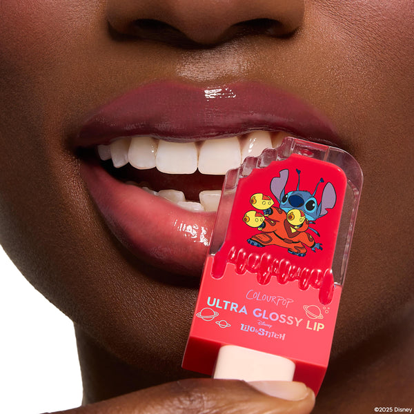 ColourPop Ultra Glossy Lip Experiment 626 tube pressed to glossy mauve lips, displaying a red popsicle-shaped container with Disney Lilo & Stitch graphic; high-shine finish and smooth texture emphasize the lip gloss’s color payoff.