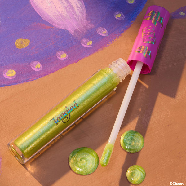 Pascal ColourPop Ultra Glossy Lip lying open with a doe-foot applicator and swirls of lime-green, gold-shimmer gloss, set on a Tangled-inspired painted backdrop, clear tube showing iridescent sheen and pink cap decorated with chameleon icons.