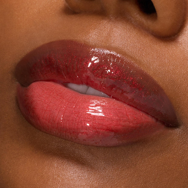 Slightly parted lips wearing ColourPop Ultra Glossy Lip in Runs with Vampires, showcasing a deep berry-red gloss with fine red shimmer and mirror shine in a macro close-up on deep skin.