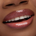Shimmering lips wear ColourPop Ultra Glossy Lip Yeehaw, a warm rosy-brown gloss with fine sparkle, reflecting light as a slight smile reveals teeth in a macro beauty shot, highlighting the high-shine, smooth finish.