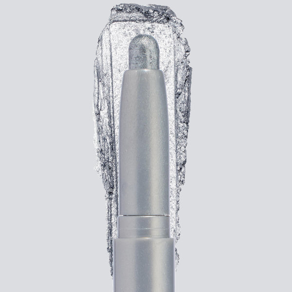 ColourPop Shadow Stix in Witch, Please showcases a creamy icy-silver shimmer, the crayon tip extended with a bold swatch behind to highlight pigment and sparkle, centered in a sleek silver tube on a light gray background.